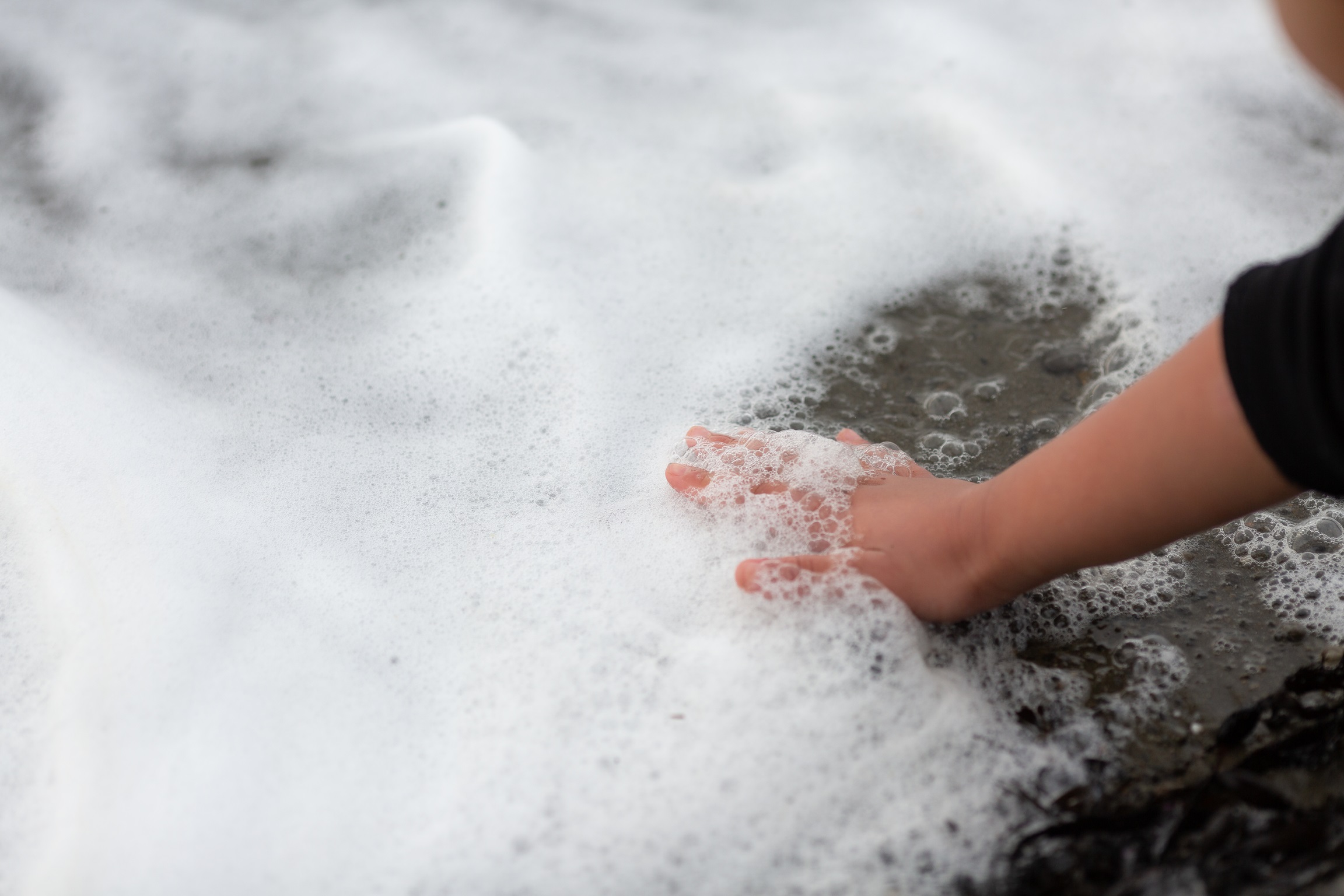 A hand touching the foam from a tide at the beach.